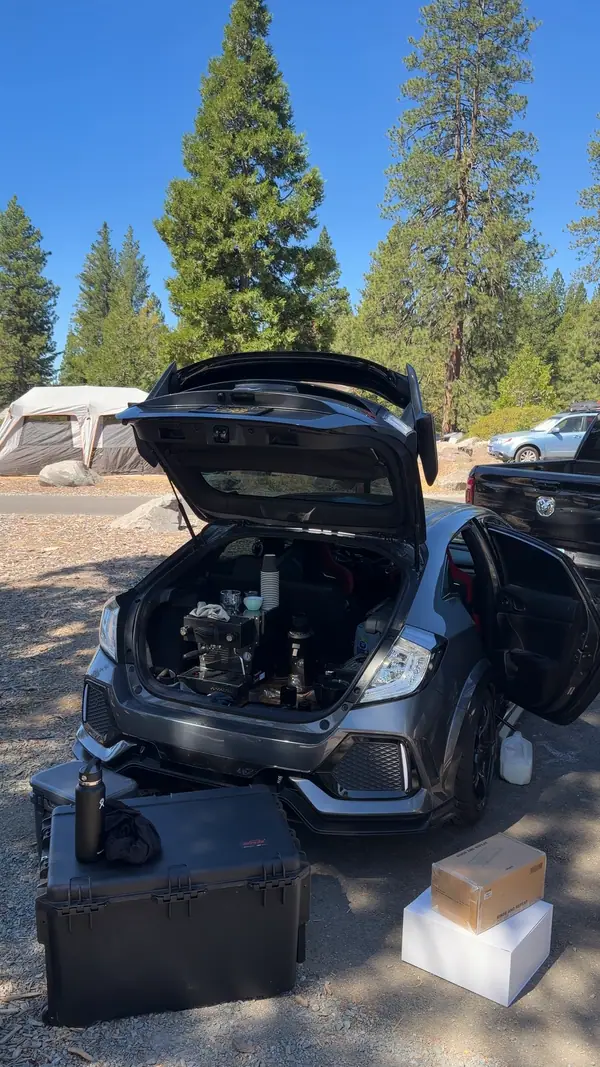 The car at a campground with the hatch open, tall pines behind