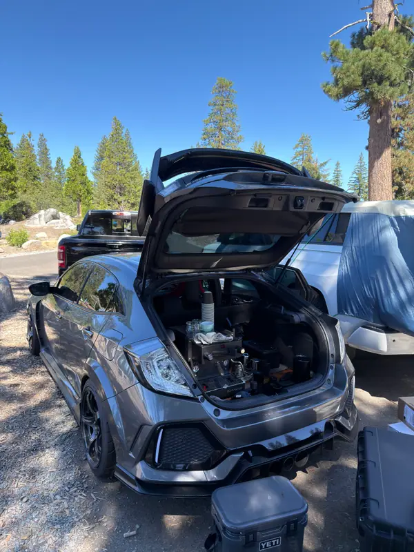 The Type R parked under the pines with its hatch up and the espresso bar inside